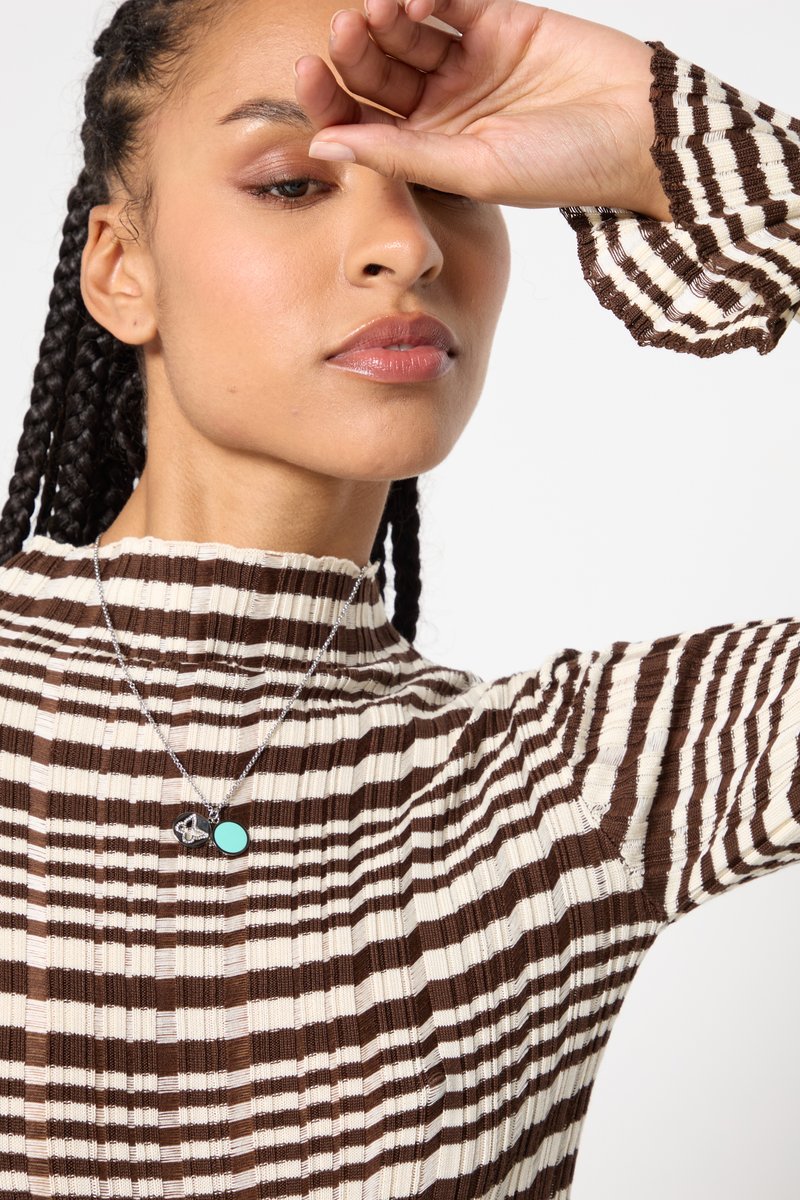 Gestreifter Stricktop in Braun und Creme, mit hohem Kragen und langen Ärmeln mit Rüschenkanten. Silberne Halskette mit türkisem Akzent.
