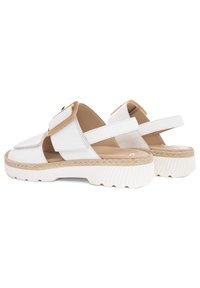 Sandalias blancas con un acabado texturizado, que presentan una gran hebilla en tono marrón claro, un respaldo abierto y una suela blanca gruesa y estriada con un acento trenzado.