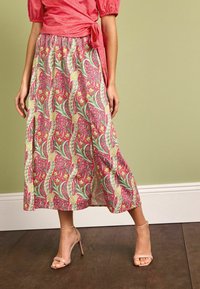 Longo gonna floreale nei toni di rosa, verde e crema con intricate fantasie di foglie e fiori. Realizzata in un tessuto leggero, presenta una scollatura laterale.