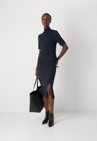 Navy turtleneck top, short sleeves, paired with a knee-length skirt featuring a side slit. Accessories include a black tote bag and ankle boots.