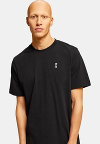 Sort kortærmet t-shirt lavet af bomuld, med et lille hvidt logo på venstre bryst. Klassisk rund halsudskæring med en afslappet pasform.