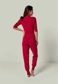 Rotes geripptes Oberteil mit Dreiviertelärmel, kombiniert mit passenden Jogginghosen. Weiche Textur, figurschmeichelndes Design und elastische Bündchen an der Hose.
