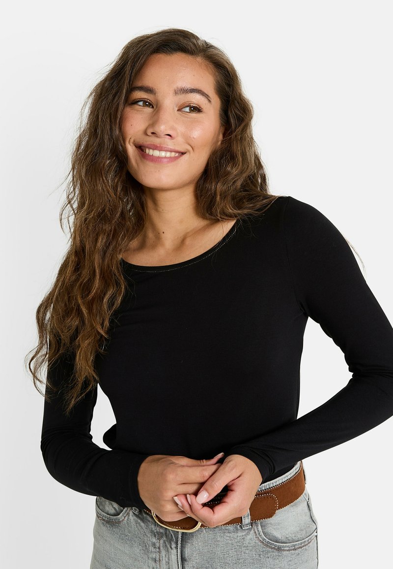 Haut noir à manches longues avec un col rond, texture lisse et design ajusté. Associé à un jean délavé et une ceinture marron.