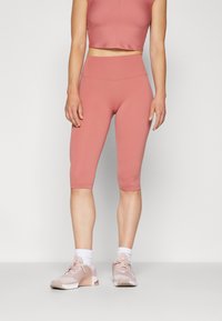 Top de sport raccourci rose et leggings capri taille haute assortis, fabriqués en matériau lisse et extensible, associés à des baskets légères et des chaussettes blanches.