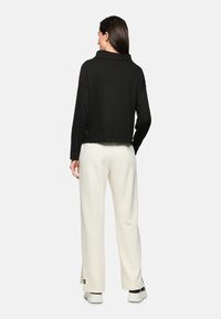 Schwarzer, kurzer Sweatshirt mit hohem Kragen, langen Ärmeln und strukturierter Oberfläche, kombiniert mit cremefarbenen, weiten Hosen und sportlichen Schuhen.