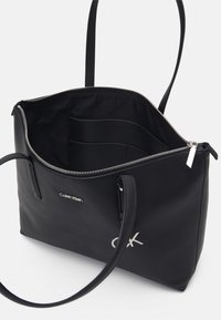 Musta nahkainen laukku vetoketjulla, tilava sisustus ja sisäiset taskut. Varustettu hopeisella logolla ja sileällä pinnalla.