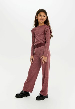 Completo due pezzi color bordeaux con maniche a volant e pantaloni larghi abbinati. Tessuto liscio e texture; abbinato a scarpe nere chunky.