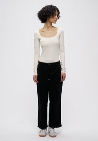 Istutettu pitkähihaisen yläosa kermaisen värisenä, jossa on neliskulmainen pääntie, yhdistettynä leveälahkeisiin mustiin housuihin ja valkoisiin lenkkareihin kuminauhapohjalla.