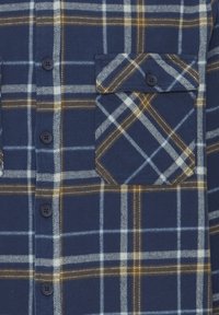 Camisa de franela a cuadros en azul marino, con rayas en azul claro, blanco y marrón. Incluye botones y un bolsillo en el pecho con un detalle de patrón.