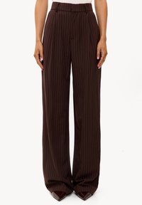 Pantalones de pierna ancha a rayas marrones con textura suave, cintura alta y calzado puntiagudo de color marrón oscuro. Corte entallado para un aspecto pulido.