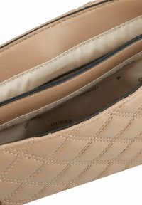 Beige gestepptes Lederinnenfach einer Tasche mit zwei Fächern und einem Satinfutter. Mit einem dezenten "Guess"-Logo auf dem Stoff.