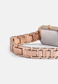 Relógio em ouro rosa com caixa retangular e bracelete de elos metálicos. Apresenta elos polidos com um acabamento suave e um mostrador simples e claro.