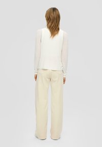 Witte langetermijn top gecombineerd met cremekleurige wijde broek. Zachte, lichte stoffen met een relaxte pasvorm en subtiele stikdetails.