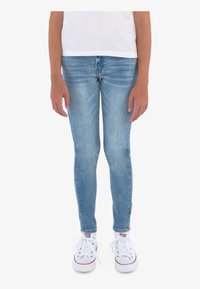 Vaaleansiniset skinny-farkut, joissa on keskipitkä vy ötärö ja sileä pinta, yhdistettynä valkoisiin kangaskenkiin.