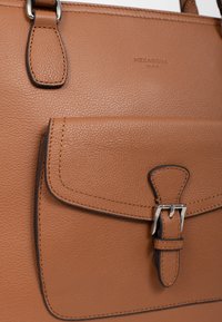 Borsa a mano in pelle marrone con finitura testurizzata, dotata di una tasca frontale con un pattino chiuso da una fibbia argentata e dettagli di cucitura in rilievo.