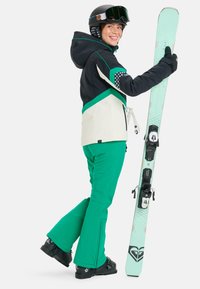 Pantalons de ski verts avec des fermetures éclairs aux chevilles, une veste blanche et noire avec des accents verts, et une planche de snowboard vert menthe avec des fixations noires.