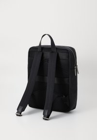 Zaino nero con materiale liscio, retro in rete imbottita, spallacci regolabili e chiusura a zip. Presenta accessori in argento e un design minimale.