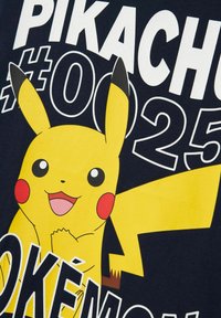 Črna majica z barvnim grafičnim prikazom Pikachuja; Pikachu je rumen z rdečimi lički, velikimi očmi in nasmejanim izrazom. Natisnjen je napis "PIKACHU #025".