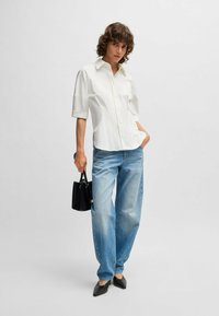 Camicia bianca con maniche corte, abbinata a jeans a gamba larga di colore azzurro chiaro. Accessoriata con una piccola borsa nera e scarpe nere a punta.