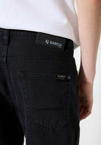Jeans in denim nero con una finitura testurizzata, dotati di due tasche posteriori e un'etichetta in pelle nera con la scritta "GARCI A EST.72."