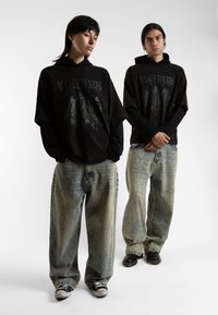 Svart oversize hettegensere med grafisk trykk, kombinert med slitte lyseblå baggy jeans. Akcenter av svarte sneakers og støvler.