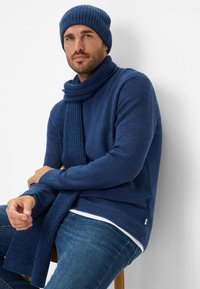 Navyblauwe geribde gebreide beanie, sjaal en trui, met een textuurafwerking en een strakke pasvorm, gecombineerd met denim jeans.