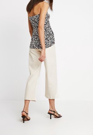 Sort-hvid leopardprint top med tætsiddende liv og uden stropper, parret med cremefarvede brede bukser og sorte strophæle.