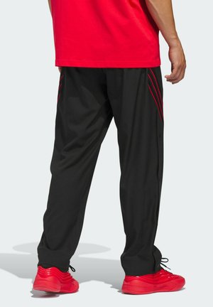Svarta träningsbyxor med röda frakturer, som har en avslappnad passform och sidoknappar. I kombination med röda sneakers och en röd skjorta.
