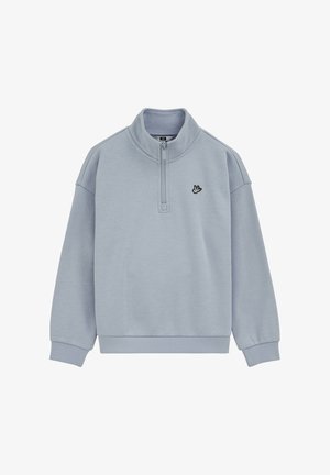 Svetlo modra majica s četrtinsko zadrgo, rebrastimi manšetami in podložnim robom, visokim ovratnikom ter majhnim črnim vezenim logotipom ptice na levi strani prsnega koša.