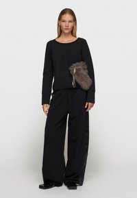 Zwarte sweatshirt met textured logo, gecombineerd met losse zwarte broek. Bevat een grijze nepbonten tas en contrasterende satijnen accenten op de broek.