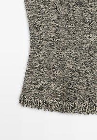 Gros plan sur un tissu tricoté chiné noir et blanc avec une texture nervurée et un détail de bord volanté sur fond blanc.