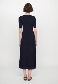 Abito a maglia a coste di colore blu navy con maniche corte e lunghezza midi. Presenta un corpetto aderente e una parte inferiore svasata con spacchi laterali.