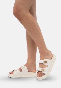Tongs blanches en matériau synthétique, dotées de deux brides ajustables avec des accents en métal doré et d'une semelle texturée.