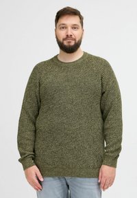 Olivgrüner Strickpullover mit Rundhalsausschnitt und Raglanärmeln; strukturiertes Muster; gerippte Bündchen und Saum; über einer hellen Jeans getragen.