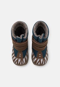Stiefel mit einem dunkeltürkisen Textil-Obermaterial, braunen Riemen und einem weißen Blattmuster auf der braunen Gummisohle. Weiche, graue Fleece-Fütterung.
