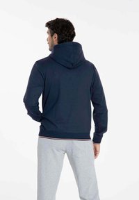 Sweatshirt bleu marine en tissu doux, doté d'une grande capuche, de poignets et d'une taille côtelés, avec une bande d'accent blanche et rouge.