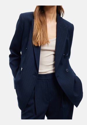 Navyblå stribede blazer med dobbeltradet knaplukning og forv pocket, parret med en beige top. Blazeren har en afslappet pasform og brede slag.