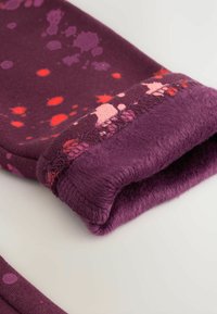 Fleecegefüttertes lila Kleidungsstück mit Spritzmustern in Pink und Rot. Die umgeschlagenen Kanten sorgen für eine weiche Textur.