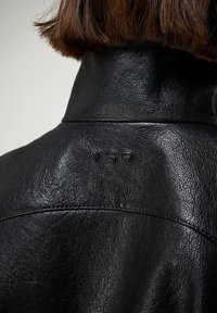 Vista trasera de una persona con cabello corto y castaño que lleva una chaqueta de cuero negra texturizada con las letras en relieve "VSP" en la parte superior de la espalda.