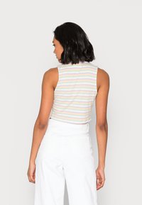 Top cropped ajustado e sem mangas em listras pastéis de rosa, azul e amarelo. Textura canelada com decote redondo. Usado com calças brancas de perna larga.