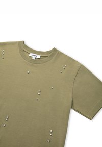 Camiseta de manga corta color verde oliva con cuello redondo, que presenta remaches metálicos dispersos en el frente y un tejido de algodón suave.