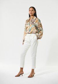 Button-up shirt with swirling brown, teal, and cream patterns; white tailored pants; brown heeled sandals; smooth fabric and structured design.
