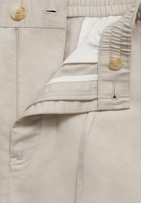 Pantalon beige en coton avec fermeture à boutons, taille élastique et une doublure intérieure lisse avec une bande contrastante.