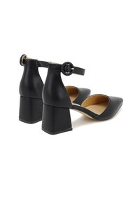 Scarpe con tacco a blocco in pelle nera, con punta affusolata e cinturino alla caviglia dotato di una fibbia circolare, texture liscia e interno color tan.