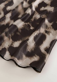 Schwarzer und beiger Stoff mit einem strukturierten Leopardenmuster, das sanft fließende Drapierungen mit einem subtilen Glanz aufweist.