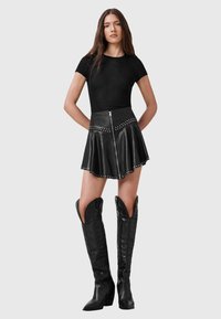 Zwart getailleerd T-shirt met korte mouwen, zwarte leren flared ritsrok met studs, knielange zwarte leren laarzen met spitse neus en decoratief ontwerp.