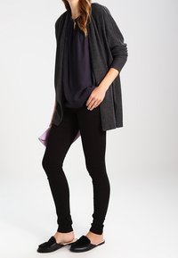 Grå öppen cardigan över en mörk topp, tillsammans med svarta skinny jeans och svarta halkskor. Enkelt design, mjukt tyg, minimal hårdvara.