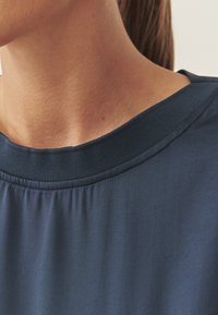 Marineblaue Bluse mit einem gerippten Ausschnitt, glatter Textur und kurzen Ärmeln, mit Fokus auf den Kragen- und Schulterbereich.