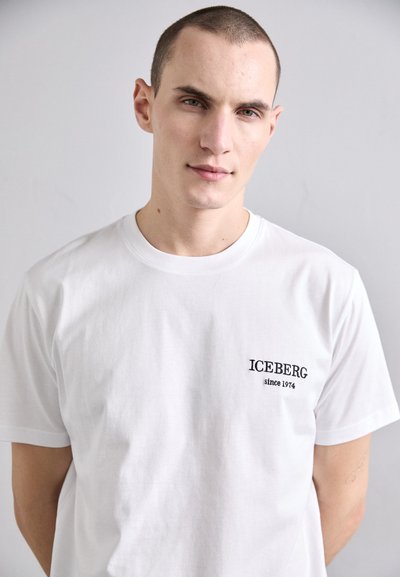T-shirt en coton blanc avec un col rond, des manches courtes et un logo brodé noir sur la poitrine gauche, indiquant "ICEBERG since 1974."