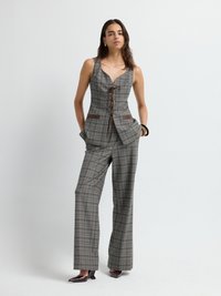 Gilet a quadri grigio con collo a V, dettagli con lacci e accenti in pelle marrone, abbinato a pantaloni a gamba larga sempre a quadri. Scarpe scure con tacco alto.